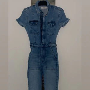 Blå jeans jumpsuit - Säljer denna väldigt fina blå jeans jumpsuit med korta ärmar och dragkedja framtill. Den har krage och två bröstfickor. Passformen är normal och materialet är skönt och slitstarkt. Använd 2 gånger max och inga slitage alls eller liknande. Inte min stil numera:) köpt för 600kr 