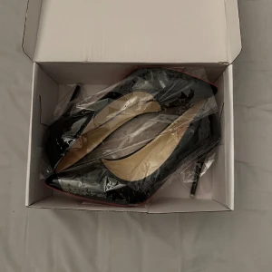 Svarta lackpumps med röd sula - Säljer ett par eleganta svarta lackpumps med en ikonisk röd sula. Skorna har en spetsig tå och en hög klack som ger en stilren och sofistikerad look. Perfekta för festliga tillfällen eller en utekväll. De är i nyskick och kommer i originalförpackning.