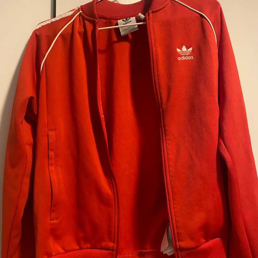 Röd adidas hoodie. En liten fläck som inte går bort längst nere på jackan som knappt syns.. Hoodies.