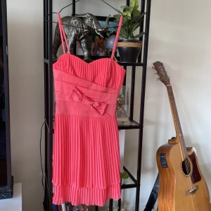 Rosa klänning med rosett - Säljer en superfin rosa klänning med smala axelband och en söt rosett framtill. Klänningen har en plisserad design som ger den ett elegant och lekfullt utseende. Perfekt för sommarens fester eller en speciell kväll ute! 💖