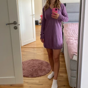 Lila klänning från Koiné - Säljer en superfin lila klänning från Koiné. Den har en v-ringad design med ribbade detaljer runt halsen och långa ärmar. Perfekt för både vardag och fest!