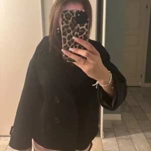 Svart kappa från Design by Si - Säljer en stilren svart kappa från Design by Si. Perfekt för höst och vinter, och passar både till vardags och fest. Kappan är i bra skick och har en normal passform.