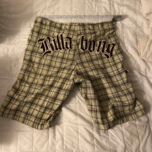 Rutig Billabong shorts - Säljer ett par rutiga shorts från Billabong i beige och svart. De har en loose passform och är perfekta för sommaren. Shortsen har en praktisk ficka på sidan och dragsko i midjan för justerbar passform. Perfekta för en avslappnad dag på stranden eller i stan!