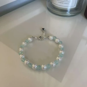 Pärlarmband med vita och blå pärlor - Snyggt armband med vita och ljusblå pärlor, perfekt för att ge en elegant touch till din outfit. Armbandet har en liten stjärndetalj vid låset som ger det en unik look. Passar både till vardags och festliga tillfällen. Ett måste för alla smyckesälskare!