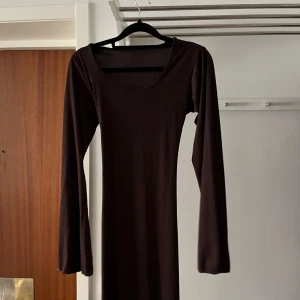 Klänning  - En brun lång klänning med snöre i bak så man kan dra åt den ifall man vill ha mer figur.  Använd 1 gång.  Jättebra kvalitet 