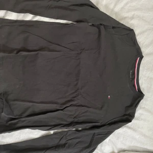 Svart långärmad tröja från Tommy Hilfiger - Säljer en stilren svart långärmad tröja från Tommy Hilfiger. Den är gjord av 100% bomull och har en liten logga på bröstet. Perfekt för både vardag och lite finare tillfällen. Passar bra till jeans eller chinos!