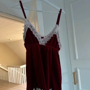 Vinrött linje med spetsdetaljer - Säljer en superfin vinrött linne med v-ringad spetsdetalj. Klänningen i sammet och har en elastisk midja för en bekväm passform. Perfekt för festliga tillfällen eller en mysig hemmakväll. Materialet känns mjukt och lyxigt.