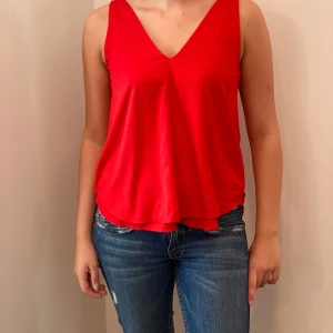 Röd ärmlös topp från Gina Tricot - Säljer en snygg röd ärmlös topp från Gina Tricot i storlek 34. Toppen har en stilren v-ringning och är perfekt för sommardagar eller festliga tillfällen. Materialet är mjukt och bekvämt, vilket gör den lätt att bära hela dagen. Passar både till jeans och kjol!