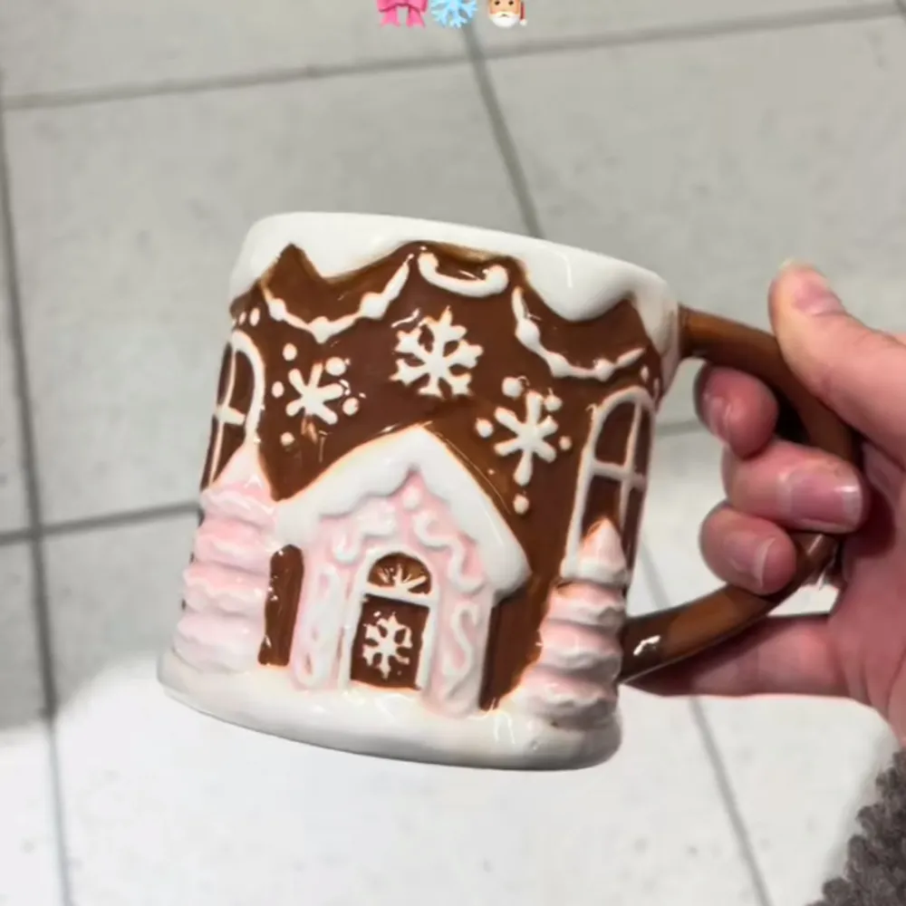 Superfin mugg som ser ut som ett pepparkakshus! Den har detaljer som snöflingor och glasyr i vitt och rosa. Perfekt för varma drycker under vintern. Handtaget är brunt och ser ut som en pepparkaksdeg. En mysig detalj för julen! 🎄☕. Övrigt.