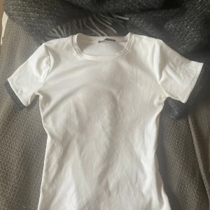 Vit t-shirt med svarta glitter detaljer från zara - Säljer en stilren vit t-shirt med svarta detaljer vid ärmsluten. Perfekt för vardagsbruk eller att styla upp med accessoarer. T-shirten har en normal passform och är kortärmad, vilket gör den idealisk för vår och sommar.