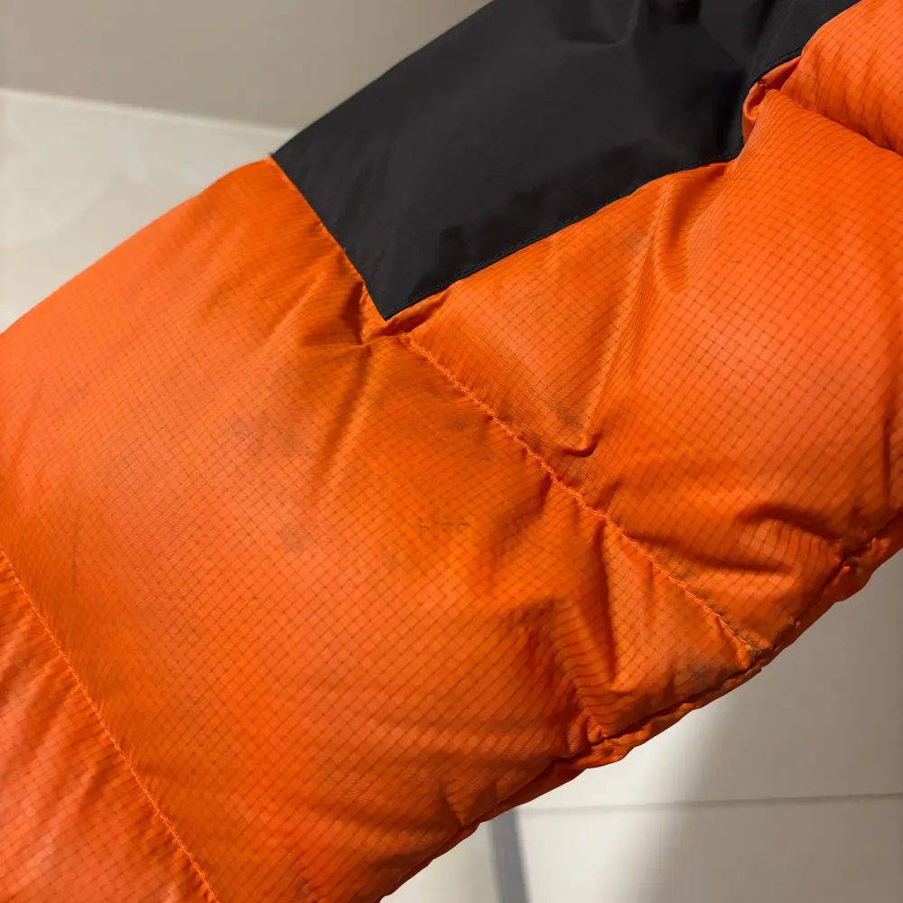 Orange dunjacka från The North Face Herrmodell Vattenavvisande ytbehandling Fickor med dragkedja Justerbar resår i nederkant Huva Innerficka Storlek M Använt i fint skick, den är hel men behöver nog en tvätt. Jackor.