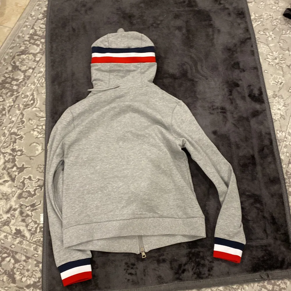 Säljer en snygg grå hoodie från Moncler i mycket bra skick. Den har en dragkedja framtill och coola ränder i rött, vitt och blått på huvan och ärmsluten. Perfekt för höst och vår när du vill vara både bekväm och stilren. Passar lika bra till vardags som till en chill festkväll.. Tröjor & Koftor.