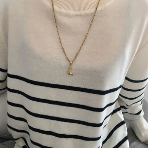 Guldhalsband med bokstavsberlock - Snyggt guldhalsband med en enkel kedja och en berlock i form av bokstaven 'L'. Perfekt för att ge en personlig touch till din outfit. Passar både till vardags och festliga tillfällen. Halsbandet är i mycket bra skick, aldrig använt och redo att bäras med stil. Det går att ta av L:et