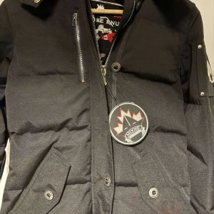 Svart pufferjacka från Moose Knuckles - Säljer en snygg svart pufferjacka från Moose Knuckles. Jackan har en dragkedja och knappar framtill, samt praktiska fickor med knappar. Perfekt för kalla dagar med sin varma vaddering. Den har också en cool detalj med en ficka på ärmen. Passar perfekt för vintern!⁉️1:1⁉️ PRIS KAN DISKUTERAS 