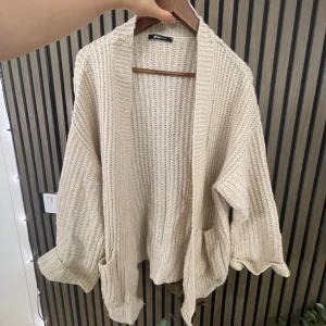 Beige stickad kofta - Mysig beige stickad kofta i oversized modell. Perfekt för kyliga höst- och vinterdagar. Den har långa ärmar och stora fickor framtill. 