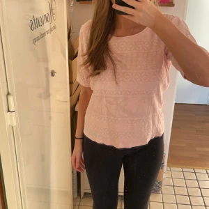 Ljusrosa mönstrad topp - Säljer en söt ljusrosa topp med ett diskret mönster. Den har korta ärmar och en rund halsringning, lite tjockare material än en vanlig T-shirt. 