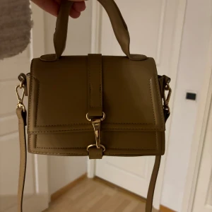 Brun axelväska med gulddetaljer - Säljer en snygg brun axelväska i skinn med gulddetaljer. Väskan har ett stilrent spänne framtill och en justerbar axelrem. Perfekt för både vardag och fest! 👜✨