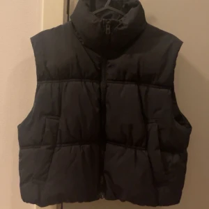 Svart pufferväst  - Säljer en svart pufferväst från H&M i storlek XS. Västen har en dragkedja framtill och är perfekt för alla säsonger. Den är i mycket bra skick och har en stilren design som passar till det mesta. Perfekt för lager-på-lager-stil!