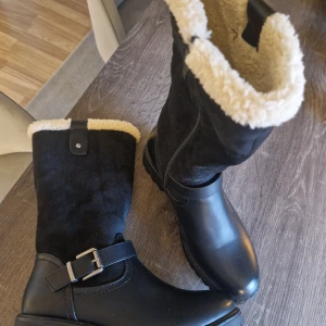 Svarta vinterstövlar med foder - Säljer ett par svarta vinterstövlar i skinn med mysigt foder. De har en snygg spänndetalj och robust sula för bra grepp. Perfekta för kalla vinterdagar! 🖤 smal modell vid foten,  dom som har 37 funkar dessa oxå för .