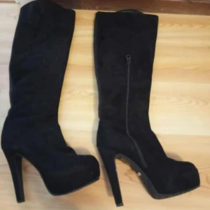 Svarta höga stövlar med klack - Snygga svarta stövlar i mocka med hög klack och dragkedja på sidan. Perfekta för en utekväll eller fest. De har en elegant och stilren design som passar till många olika outfits.