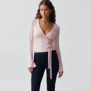 Rosa omlottopp - Säljer en superfin rosa omlottopp med lång ärm och knytning i midjan. Toppen har en v-ringad design som ger en elegant look. Perfekt för både vardag och fest!