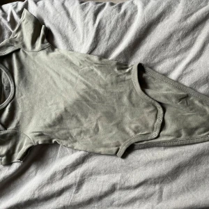 Grön kortärmad body från H&M - Säljer en söt grön kortärmad body från H&M i ekologisk bomull. Perfekt för små äventyrare! Den har praktiska knappar i grenen för enkel på- och avklädning. Passar barn i åldern 12-18 månader.