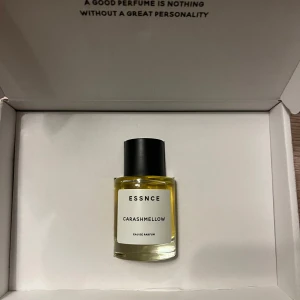 Essnce Carashmellow Eau de Parfum - Säljer en flaska Essnce Carashmellow Eau de Parfum. Den kommer i en stilren glasflaska med svart kork och en enkel vit etikett. Doften är söt och krämig, perfekt för dig som älskar mjuka och inbjudande parfymer. Flaskan ligger i en elegant förpackning med texten 'A good perfume is nothing without a great personality'.