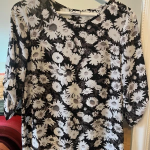 Blommig klänning med trekvartsärm - Säljer en superfin blus med svart och vitt blommönster. Den har trekvartsärmar och är perfekt för både vardag och fest. Materialet känns lätt och luftigt, vilket gör den skön att bära hela dagen. 