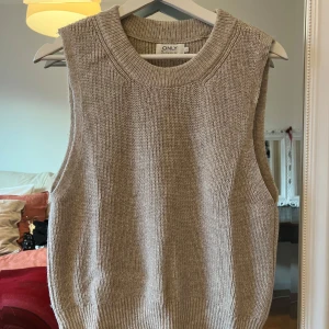 Beige stickad väst från ONLY - Säljer en snygg beige stickad väst från ONLY. Perfekt för lager-på-lager under hösten eller våren. Den har en ribbad kant vid ärmhålen och nederkanten för en stilren look. Passar bra till både skjorta och t-shirt. 