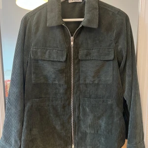 Grön manchesterjacka från Pieces - Säljer en snygg grön manchesterjacka från Pieces. Jackan har en dragkedja framtill och två stora fickor på bröstet. Perfekt för höst och vår med sin stilrena look och bekväma passform. Passar både till vardags och lite finare tillfällen. 