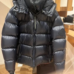 Navy blå pufferjacka från J. Lindeberg  - Säljer en snygg svart pufferjacka från J. Lindeberg. Den är perfekt för vintern med sitt quiltade mönster och långa armar. Jackan har en hög krage för extra värme. Den är i mycket bra skick och redo för kalla dagar! 🖤 Samt öppen för byten och priset kan diskuteras!