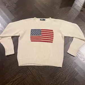 Säljer en snygg beige stickad tröja från Polo Ralph Lauren med en amerikansk flagga på framsidan. Tröjan är i bomull och har långa ärmar, perfekt för höst och vår. Den enda märkbara skavanken är ralphlaurentaggen med storlek som är lös på höger sida. Skriv om du har frågor!