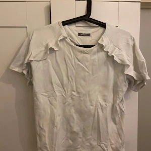 Vit topp från Gina tricot  - Säljer en söt vit topp från Gina Tricot med volangdetaljer längs ärmarna. Toppen är i bra skick och har en normal passform. Passar till både jeans och kjol för en stilren outfit.💕