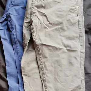 Beige och blå byxor från Zara Man - Säljer två par byxor från Zara Man Basic Collection. Ett par är beige och det andra är blått. Perfekta för både vardag och lite mer uppklädda tillfällen. De har en normal passform och är tillverkade i bomull för en bekväm känsla. Passar bra till både vår och höst.