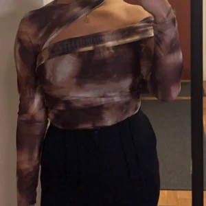 Brun mönstrad oneshoulder topp - Snygg brun mönstrad oneshoulder body med en unik design. Toppen har en cool asymmetrisk stil och är perfekt för en utekväll. Materialet ser ut att vara stretchigt och bekvämt, vilket ger en tight passform. Perfekt för att sticka ut på festen! Ny endast provad ,storlek large men passar även en s/ m då den är stretchiga 