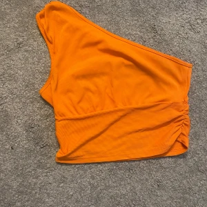 Orange oneshoulder topp - Säljer en snygg orange oneshoulder topp i ribbat material. Toppen har en tight passform och är superbekväm. Färgen är snyggare i verkligheten. Köptes för 80 kr