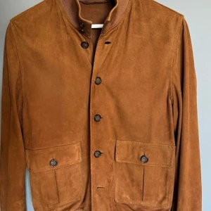 Valstar ”Valstarino” mockajacka  - Nypris 15000kr Strl 48   Superfint skick av Valstars ikoniska jacka Valstarino!   Tillverkad i mjuk getmocka är den en moderniserad klassiker som kombinerar sportig stil med elegans. Ett måste i varje modemedveten mans garderob!   Utvecklad 1935 som ett svar på den ikoniska A1-flygjackan, är Valstarino Valstars signaturdesign som har fått fans över hela världen. Den har förblivit trogen originalet med fem knappar fram, ribbade muddar och fåll samt fickor med knäppning. Denna version är tillver