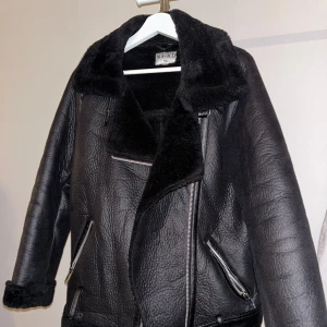 Svart skinnjacka från NA-KD - Säljer en snygg svart skinnjacka från NA-KD i mycket bra skick. Jackan har en cool bikerstil med dragkedja och mjukt foder, tillsammans med ett bälte. Perfekt för höst och vinter, den håller dig varm och stilren. Storleken är dam XS. Passar perfekt till både vardag och fest! Oversized stil! Har mindre skavank men som kan fixas.