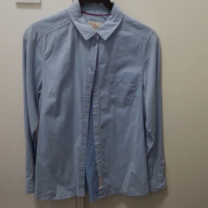 Ljusblå skjorta från Holly & Whyte - Säljer en stilren ljusblå skjorta från Holly & Whyte by Lindex. Skjortan har en klassisk krage och långa ärmar med knappar vid ärmsluten. Perfekt för både vardag och festliga tillfällen. Den är i mycket bra skick och passar till alla säsonger.