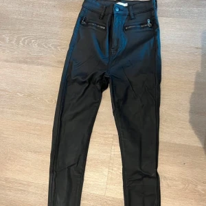 Svarta skinny byxor med dragkedja - Snygga svarta skinny byxor i syntetmaterial med hög midja. De har coola dragkedjor framtill och en stilren design. Perfekta för både vardag och fest! Använd endast 1 gång. 