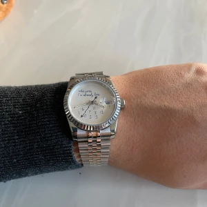 Silverfärgad klocka med text - Säljer en stilren silverfärgad klocka med ett unikt budskap på urtavlan: 'Who cares I'm already late'. Klockan har en klassisk design med en metallarmband och en vit urtavla. Perfekt för den som vill ha en rolig och avslappnad stil. Kommer med ett snyggt brunt fodral och verktyg för justering. Skriv för frågor och prisförslag 