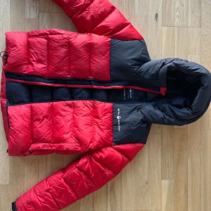 Röd och svart dunjacka från Sail Racing - Säljer en snygg och varm röd och svart dunjacka från Sail Racing - Cloud down hood. Väldigt lätt men väldigt varm. Funkat fint de kallaste vinterdagarna. Ska vara storlek small för män men funkar unisex. Sitter bra på min son 13-14år som har 170cl just nu men funkade även bra för ett år sedan när han hade 164cl. Kan inte hitta något hål eller märke på jackan.