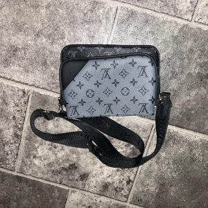 Axelväska med monogrammönster - Snygg axelväska med klassiskt monogrammönster i svart och grått. Väskan har en justerbar axelrem och två separata fack med dragkedja. Perfekt för både vardag och fest!OBS! Pris kan diskuteras