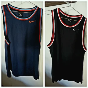 Två sportiga linnetoppar från Nike - Säljer två snygga och sportiga linnetoppar från Nike. Den ena är mörkblå med orange och blå detaljer, och den andra är svart med vita och röda detaljer. Perfekta för träning eller en varm sommardag. Båda är i mycket bra skick och har en bekväm passform.