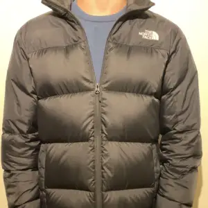 Säljer en svart dunjacka från The North Face i mycket bra skick. Jackan har en dragkedja framtill och är perfekt för kalla vinterdagar. Den är långärmad och har en klassisk pufferstil som håller dig varm och bekväm. Perfekt för både vardag och utomhusaktiviteter!     Jackan är helt äkta köpt på stadium förra vintern! 