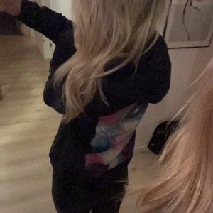 Svart hoodie med färgglatt ansiktsmotiv - Säljer en svart hoodie från The Cool Elephant med ett stort, färgglatt ansiktsmotiv på ryggen. Den har en normal passform och är perfekt för höst och vår. Hoodien är i bra skick och har en liten logga på bröstet.💕💕