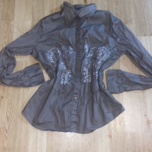 Grön/Grå skjorta med ett jättefint mönster !! - Säljer en snygg grön/grå blus från Mitno med vackra vita broderier framtill. Blusen har långa ärmar och knappar hela vägen ner. Perfekt för både vardag och fest! 💫