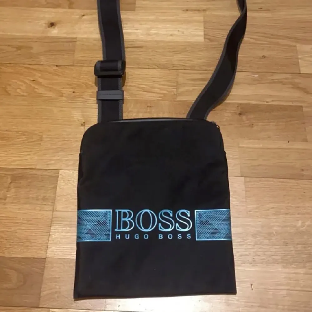 Snygg svart axelväska från Hugo Boss med justerbar rem. Perfekt för vardagsbruk med stilren design och tydlig logga i blått. Väskan är i mycket bra skick och passar till alla tillfällen. Byten funkar också.. Laukut & Käsilaukut.