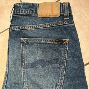 Blå jeans från Nudie Jeans - Säljer ett par snygga blå jeans från Nudie Jeans i bra skick. De har en klassisk femficksdesign och en bekväm passform. Helt nya, skick 10/10, storlek 30/32 hör av er vid funderingar!