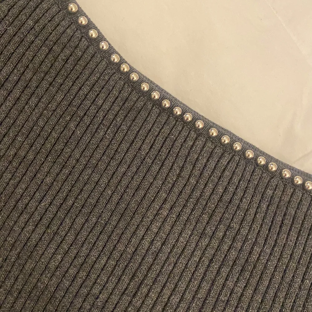 Säljer en stilren grå ribbad tröja från H&M i storlek M. Tröjan har långa ärmar och en snygg detalj med pärlor längs halsringningen. Perfekt för både vardag och fest! 🖤. Neuletakit & Villapaidat.